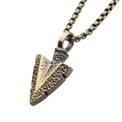 A detailed close-up image showcases the "Antiqued Gold IP Arrowhead Pendant with Bold Box Chain" by INOX. The arrowhead-shaped pendant, featuring a textured surface, hangs elegantly from a prominent box chain with an alternating link pattern. Together, the chain and pendant emanate a rugged, antique charm.