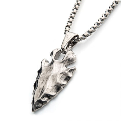 A close-up image of the Brushed Steel Chiseled Arrowhead Pendant with Box Chain by INOX features a finely detailed arrowhead pendant. The sturdy men's pendant dangles from a chain made of interconnected rectangular links, giving the piece a stylish and robust appearance.