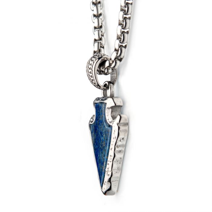 Close-up of the INOX men's Lapis Lazuli Stone with Polished Steel Frame Pendant, shaped like an arrowhead and hanging from a 24-inch polished steel box chain. The jewelry features detailed carving along the edges of the blue stone and a small, decorative loop connecting it to the polished steel frame.